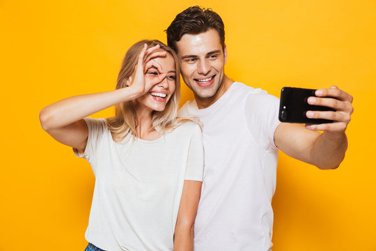 Young loving couple standing isolated over yellow wall background take a selfie by mobile phone.