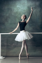 The classic ballet dancer in white tutu posing at ballet barre on studio background. Young teen before dancing. Ballerina project with caucasian model. The ballet, dance, art, contemporary