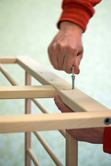 Joiner collects a new baby cot with a hand tool. The man is picking up a children's wooden crib. Waiting for the baby.