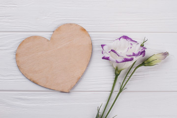 Lisianthus eustoma flower and wooden heart. Love and valentines day concept. White wooden background.