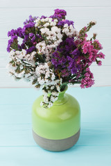 Multicolored statice limonium flowers in a green ceramic vase. Blue wooden background.