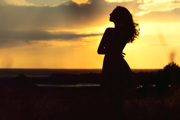 silhouette of girl at sunset in summer field, a young woman enjoying nature
