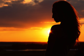 silhouette of a beautiful girl at sunset in a field, face profile of young woman enjoying nature