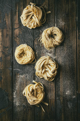 Variety of italian homemade raw uncooked pasta spaghetti and tagliatelle with semolina flour over dark plank texture wooden table. Flat lay, space