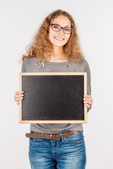 Young casual woman holding a blackboard and presenting on it while smiling for the camera. on white background