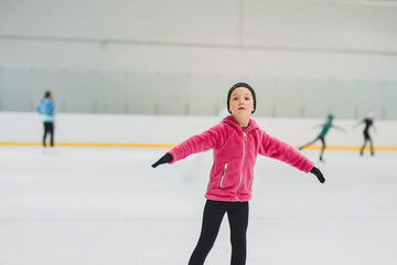Little girl learning to ice skate. Figure skating school. Young figure skater practicing at indoor skating rink. © alexngm