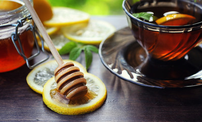 Tea with lemon and mint in nature. A cup of hot mint tea with lemon and honey in a jar. Lemon slices and a spoon with honey to hot tea.