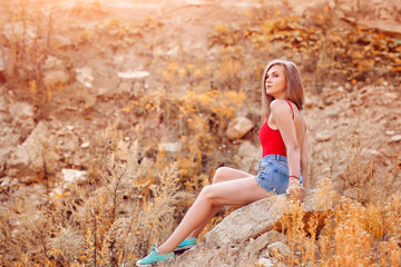 Beautiful young woman sitting on the rock, in the afternoon, in hot weather