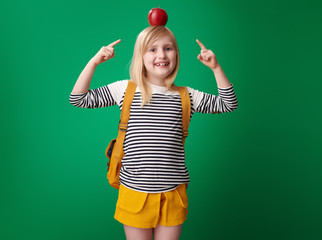 school girl pointing at apple on head against green background