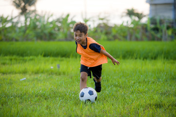 8 or 9 years old happy and excited kid playing football outdoors in garden wearing training vest...