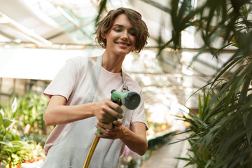 Woman gardener standing over plants in greenhouse water flowers