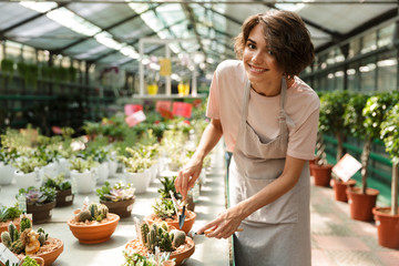 Naklejka na ściany i meble Cute woman gardener standing over flowers plants in greenhouse working