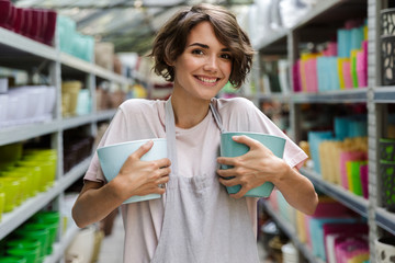 Woman gardener standing in greenhouse choosing vase pot for plants.