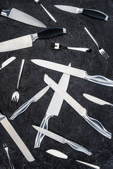 top view of various kitchen knives and forks arranged on black surface