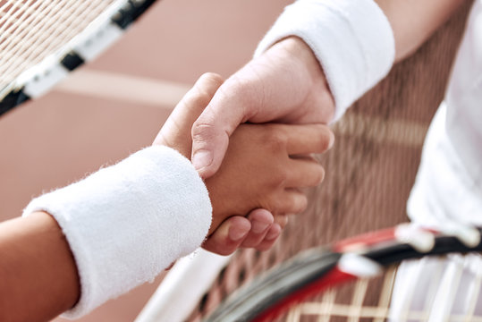 Shaking hands after good game. Close-up of man and woman in wristband shaking hands upon the tennis net