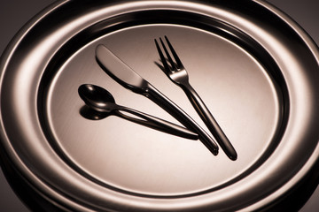 close-up view of spoon, fork and knife on shiny plate on grey