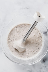 prepare batter for pancakes in a glass bowl with a hand blender on a marble table