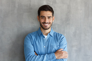 Fototapeta premium Horizontal shot of handsome Caucasian guy pictured isolated on grey background standing with arms crossed in casual clothes, looking confident and optimistic, smiling friendly and happily while posing