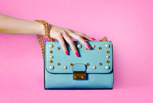 Sky blue handbag purse and beautiful woman hand with red manicure isolated on pink background.