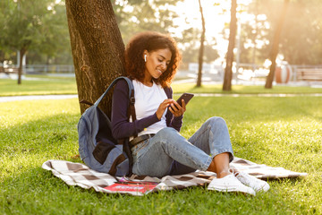 Young woman sitting outdoors in park using mobile phone.