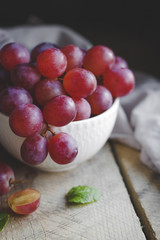 Bowl with pink grapes on a wooden stand.