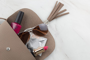 Obraz premium top view contents of women bag condom,lipstick ,nail polish and sunglasses in an open bag on the marble table