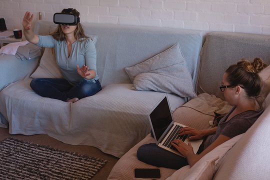 Lesbian couple using virtual reality headset and laptop on sofa
