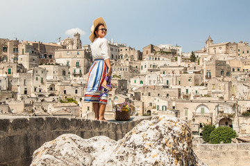 Young elegant woman tourist in historical Matera town in Italy standing on a wall looking at city landscape - obrazy, fototapety, plakaty