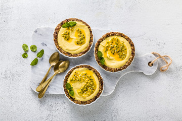 vegan raw mini tarts from nuts and dates with cashew cream from mango purée with lime juice and seeds of passion fruit. healthy alternative food on a white marble board