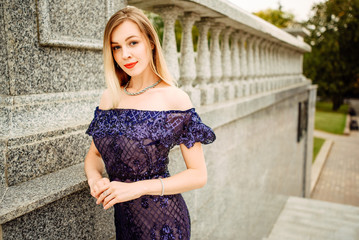 Fashionable portrait of style. Young beautiful woman in a blue long dress posing on the stairs against the old city building.The girl is outdoors