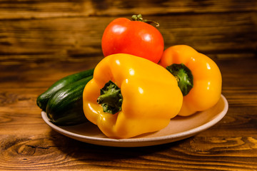 Ceramic plate with cucumbers, tomatoes and sweet pepper on wooden table