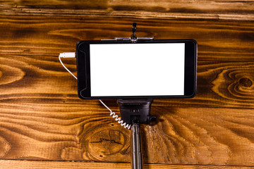 Selfie stick with modern smartphone on a wooden table