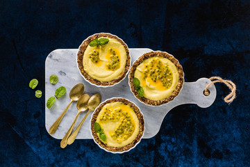 vegan raw mini tarts from nuts and dates with cashew cream from mango purée with lime juice and seeds of passion fruit. healthy alternative food on a blue background