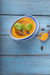 Pumpkin cream soup with pumpkin seeds, pumpkin oil and turmeric on a blue background. Top view. Free space