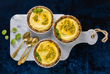 vegan raw mini tarts from nuts and dates with cashew cream from mango purée with lime juice and seeds of passion fruit. healthy alternative food on a blue background