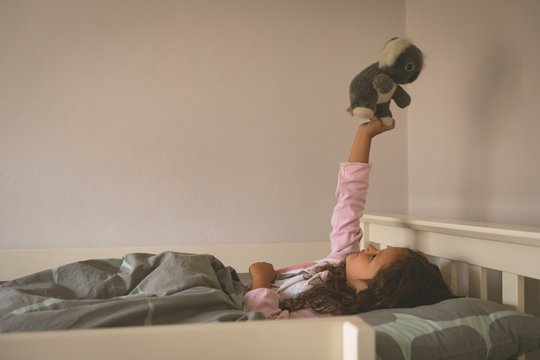 Girl playing with teddy bear on bed 
