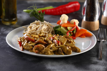 chicken with curry sauce with spaghetti and vegetables on a wooden background