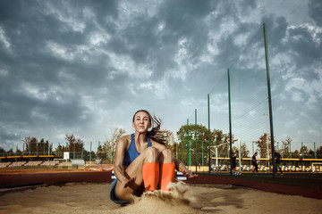 Female athlete performing a long jump during a competition at stadium. The jump, athlete, action,...