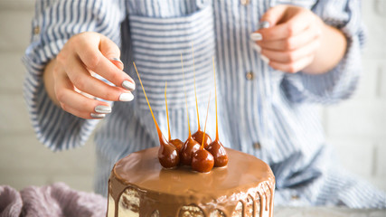 A confectioner is decorating a ready-made cake, poured with chocolate, using caramel ornaments. Confectionery