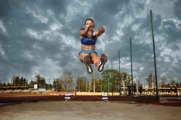 Female athlete performing a long jump during a competition at stadium. The jump, athlete, action,...