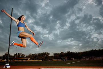 Female athlete performing a long jump during a competition at stadium. The jump, athlete, action,...