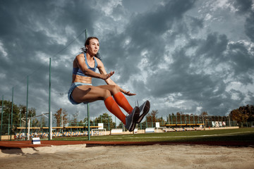 Female athlete performing a long jump during a competition at stadium. The jump, athlete, action,...