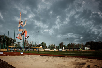 Female athlete performing a long jump during a competition at stadium. The jump, athlete, action,...