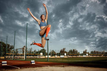 Female athlete performing a long jump during a competition at stadium. The jump, athlete, action,...
