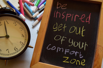 be inspired get out of your comfort zone on phrase colorful handwritten on chalkboard, alarm clock with motivation and education concepts
