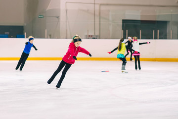 Little girl learning to ice skate. Figure skating school. Young figure skater practicing at indoor skating rink. - obrazy, fototapety, plakaty