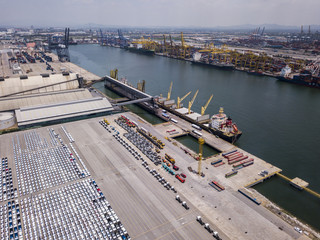 Aerial view of logistics concept floating dry dock servicing cargo ship and commercial vehicles, cars and pickup trucks waiting to be load on to a roll-on/roll-off car carrier ship at Laem Chabang 