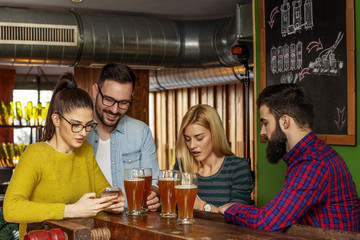 Four friends looking at mobile phone on local pub with beer on table