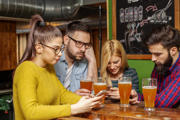 Four friends looking at mobile phone on local pub with beer on table