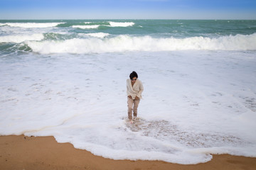 Asian woman wearing robe playing foam wave on the beach in sunshine day